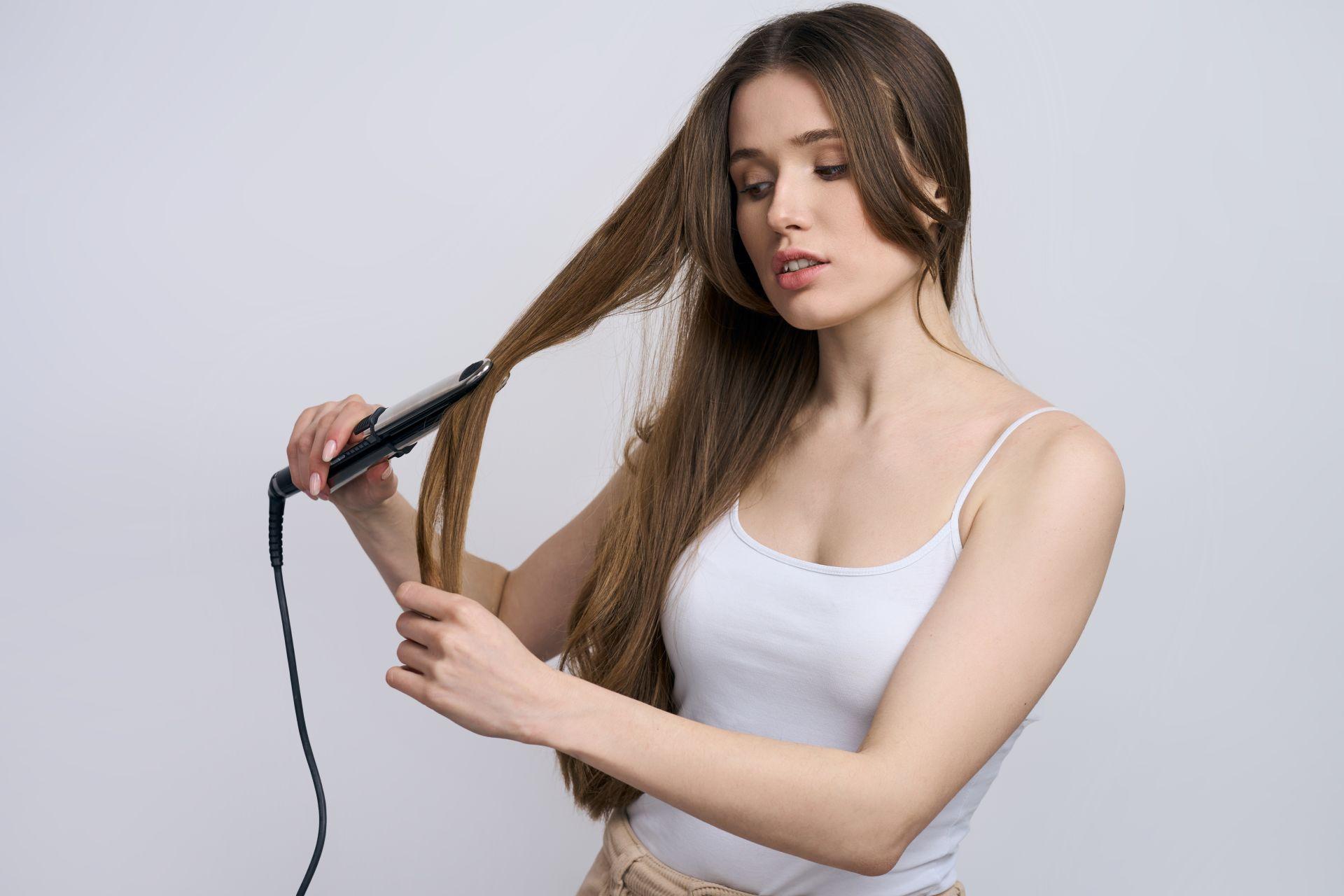 Frau glättet ihre langen Haare mit einem Glatteisen – Haarpflege mit Tape In Extensions